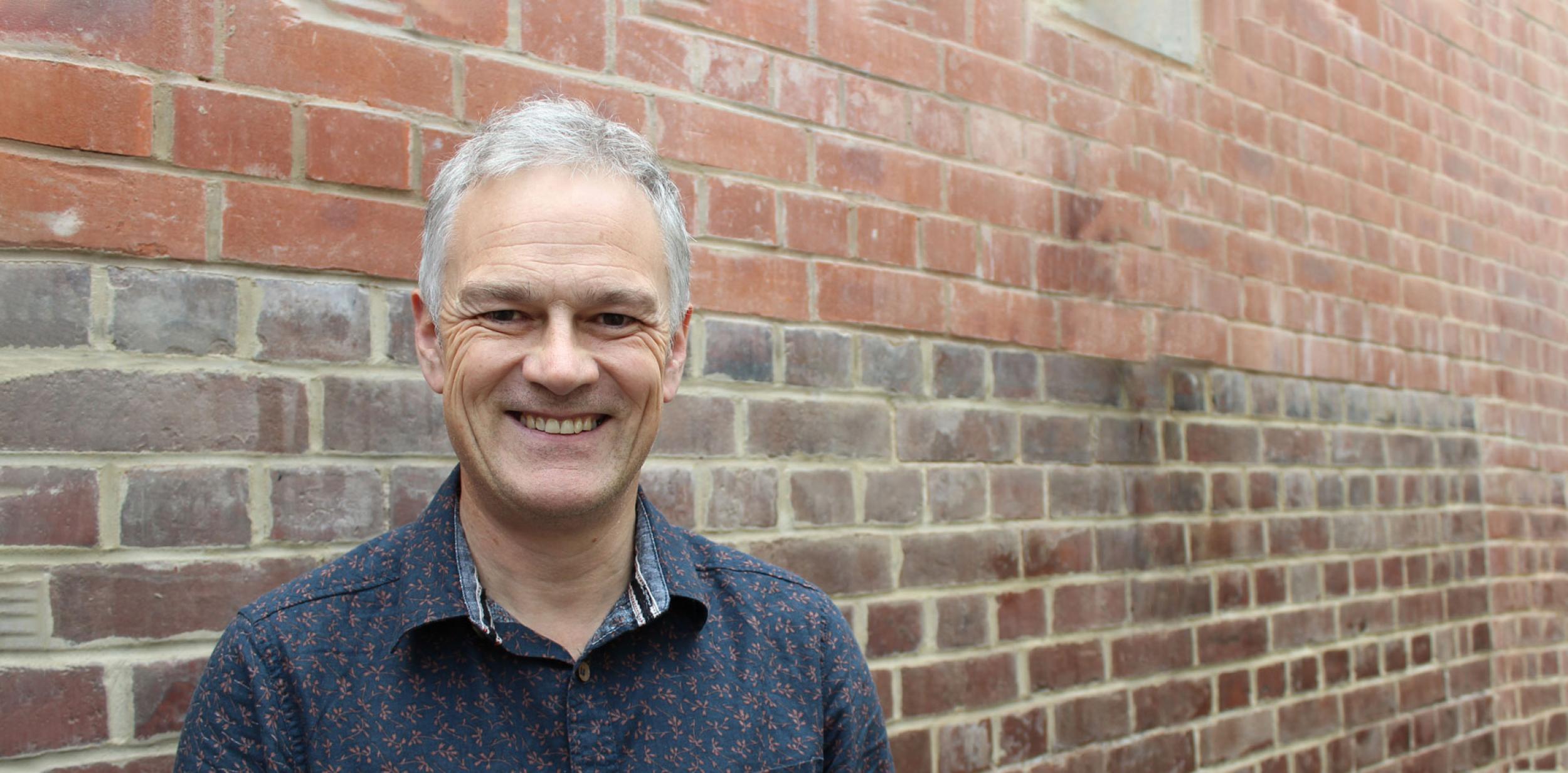 Deryck Newland standing in front of a brick wall.