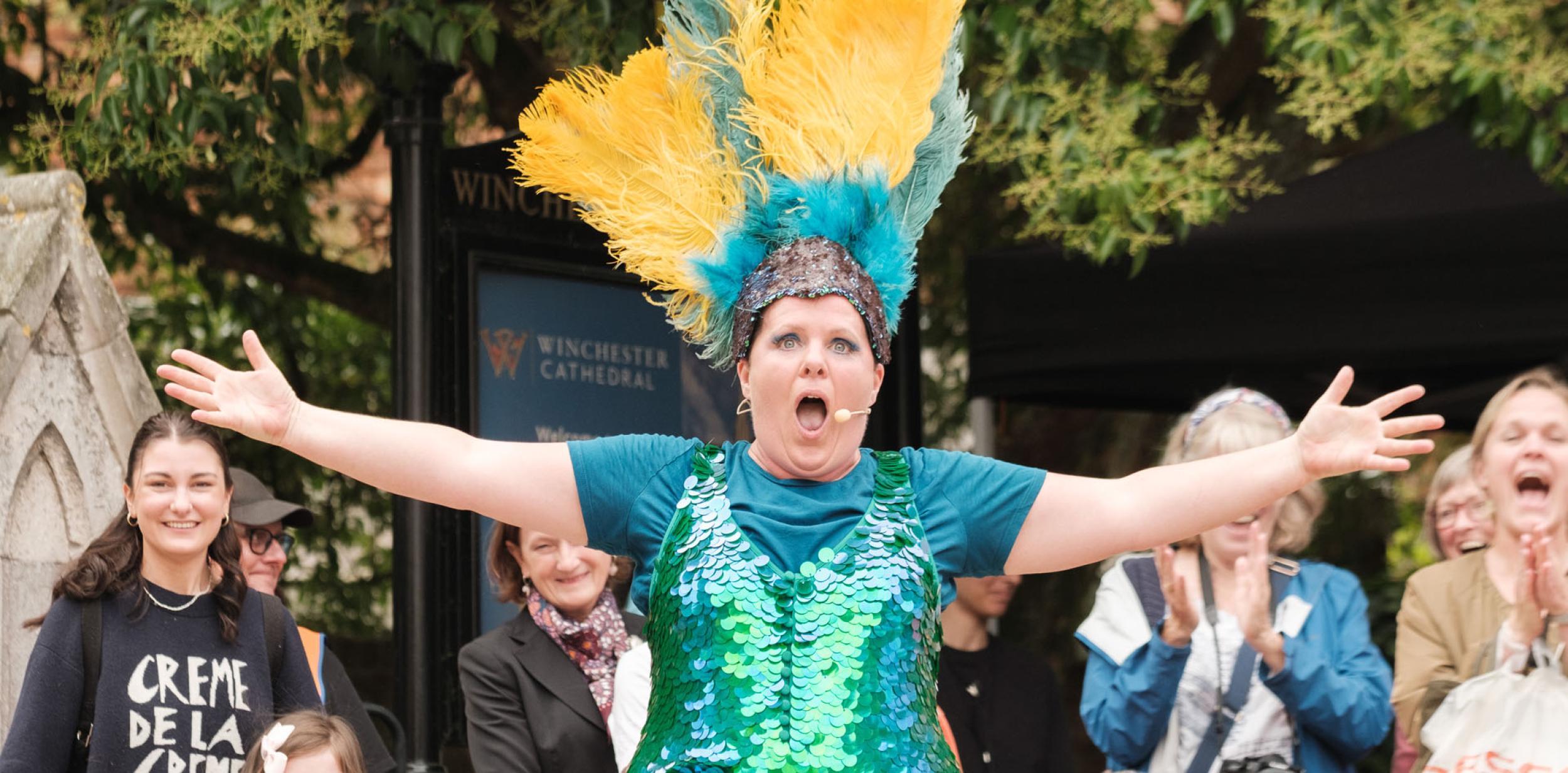 A performer in a sparkly costume and headdress performing to an audience outdoors