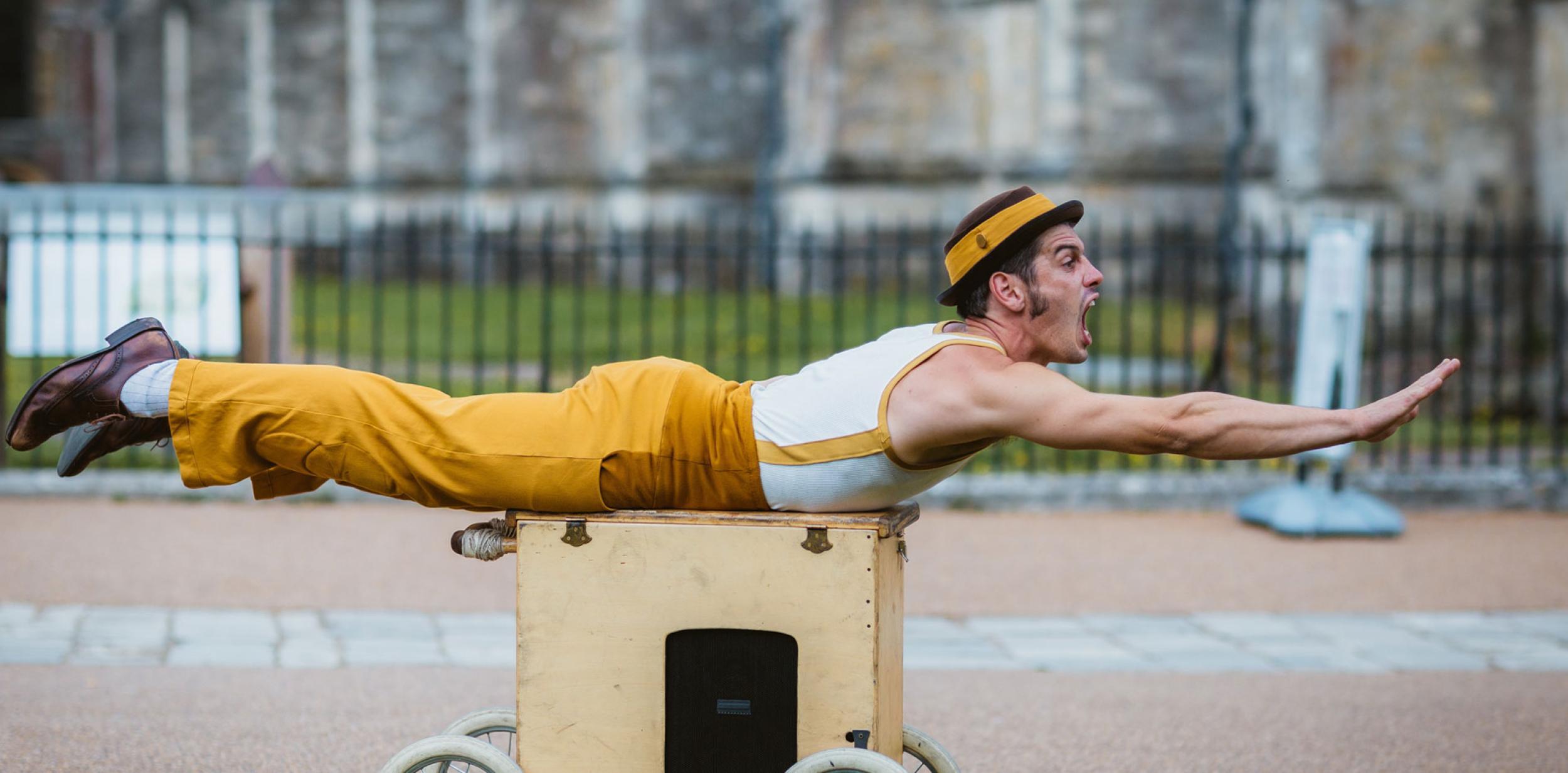 A man lying on his front on a box on wheels, doing a superman pose