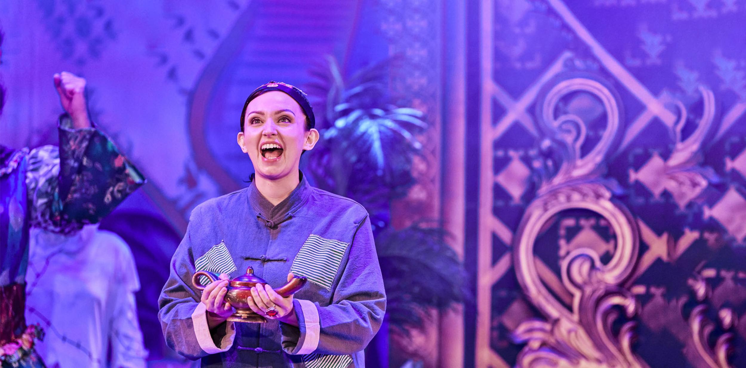 Actor playing Aladdin looking please and holding a lamp