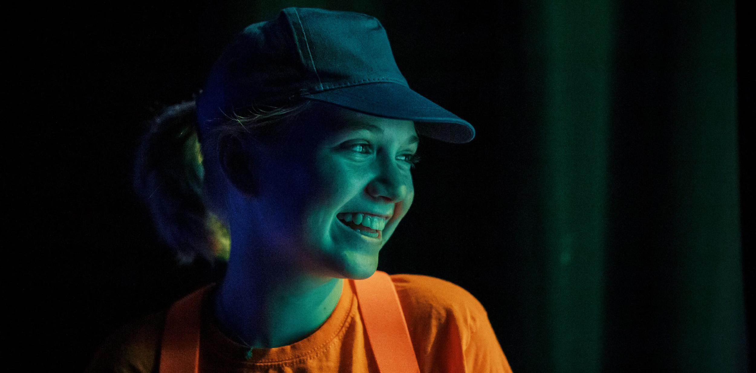 Young girl in bright orange top, smiling and enjoying being on stage.