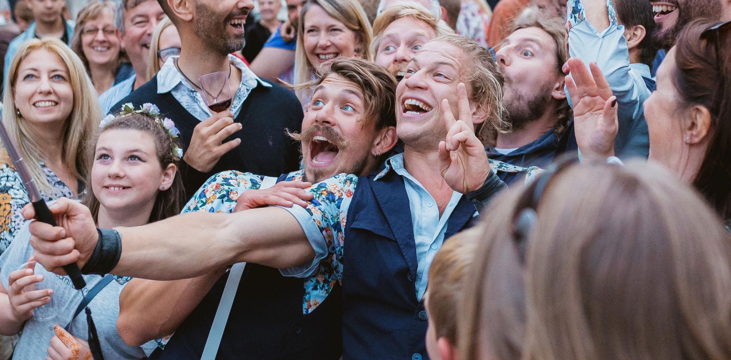 Performers taking a selfie with a huge smiling crowd of people.