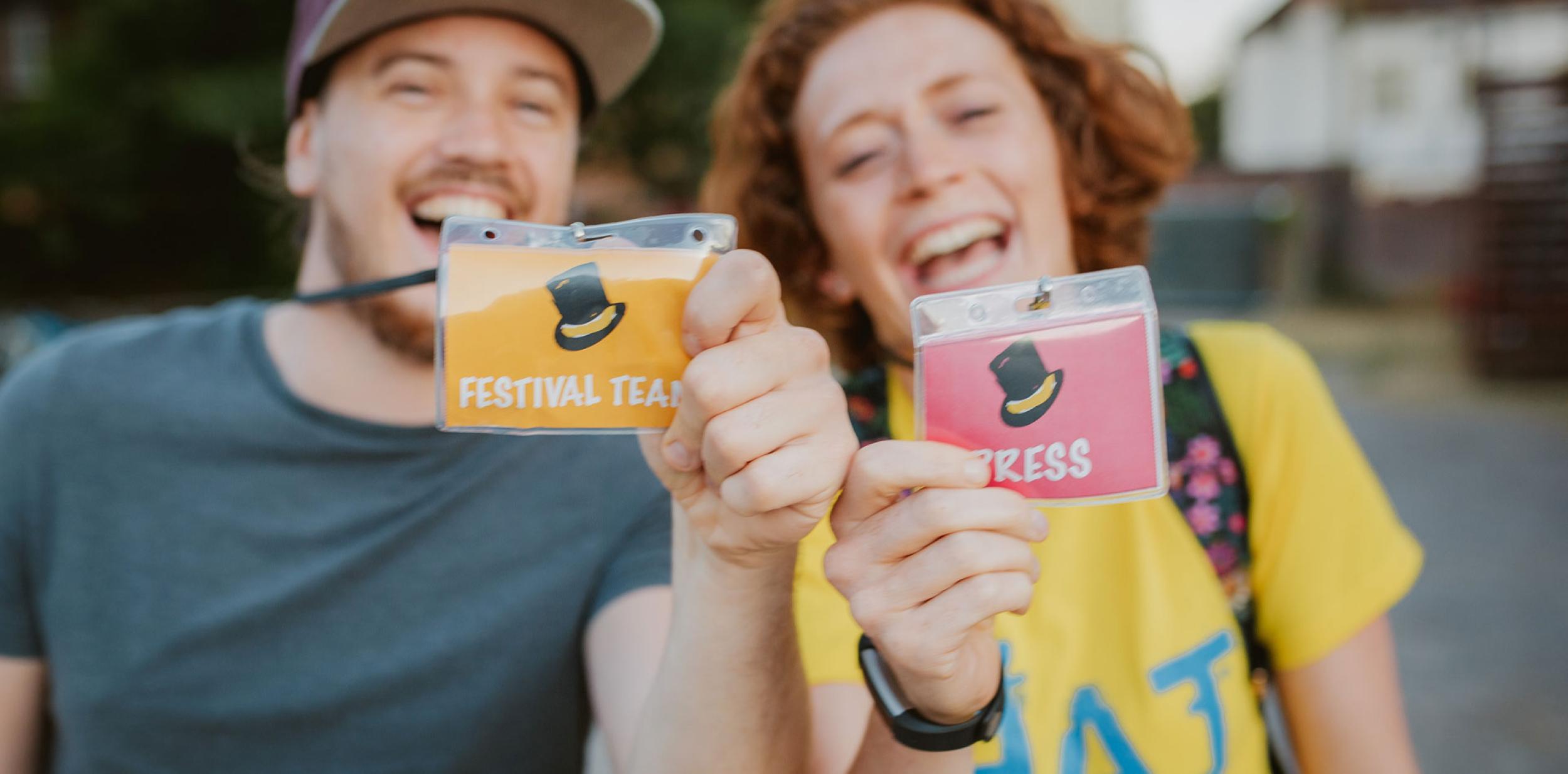 Two smiling people holding press passes up to the camera