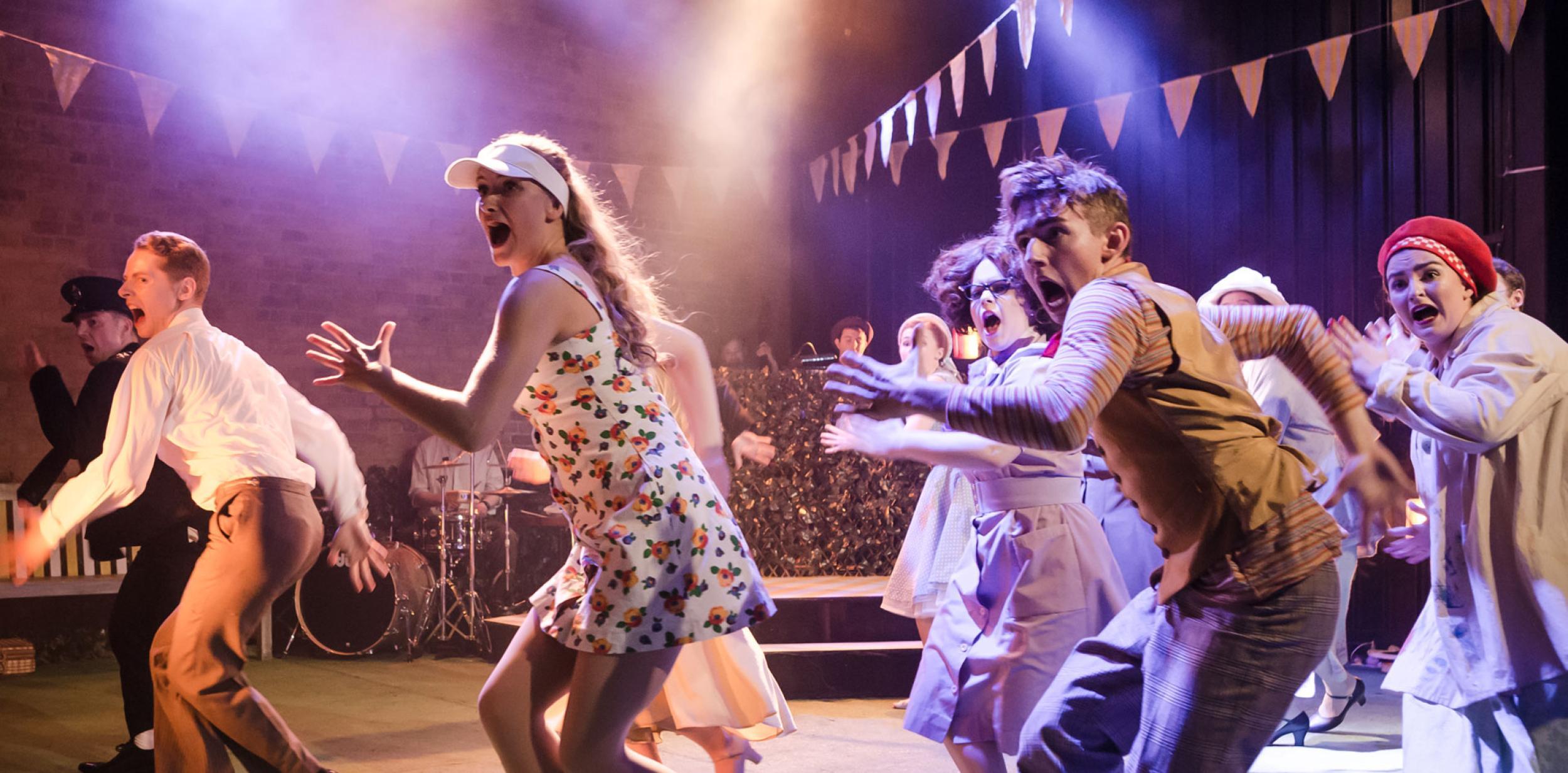 A group of people dancing on stage under multi-coloured lighting