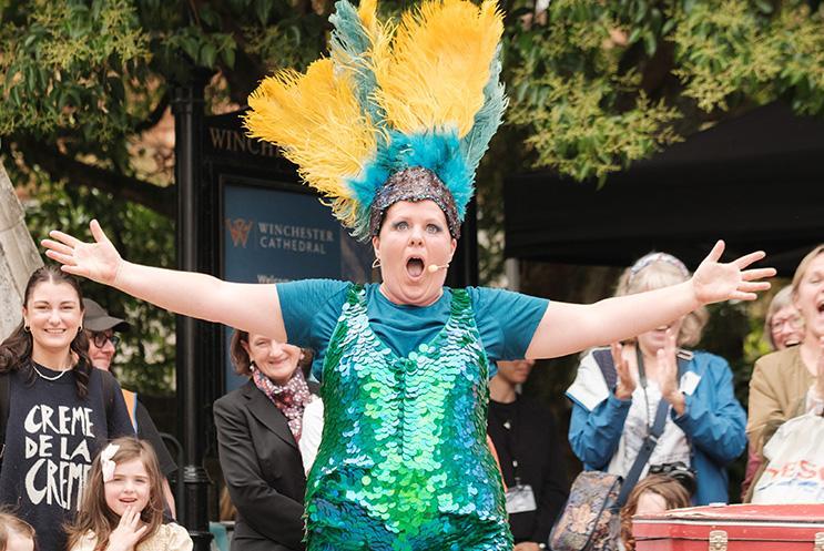 A performer in a sparkly costume and headdress performing to an audience outdoors