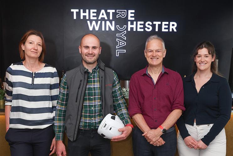 A group stood in front of the Theatre Royal Winchester illuminated logo.