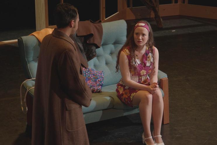 Young woman sat on sofa on stage talking to a young man