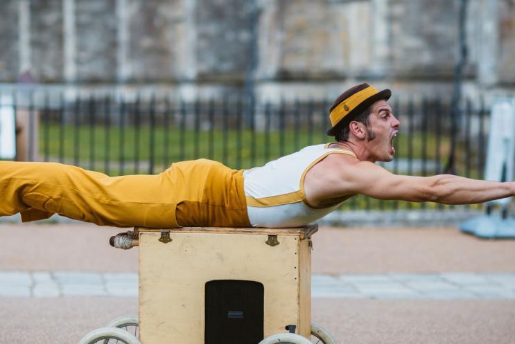A man lying on his front on a box on wheels, doing a superman pose