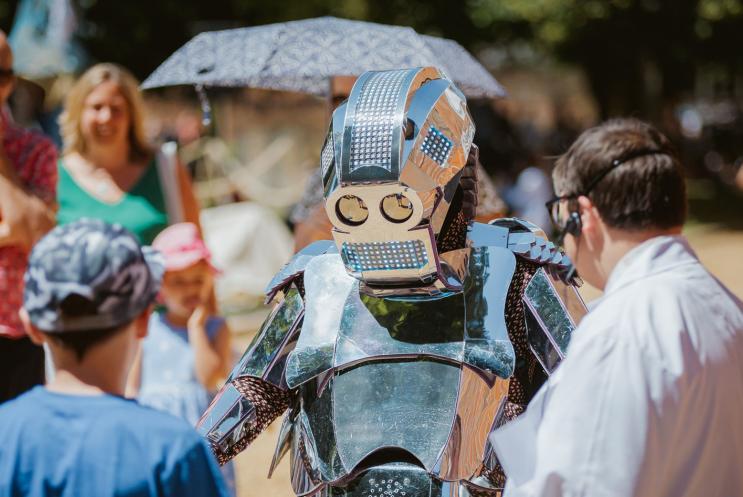 Performer at Hat Fair 2018 Outdoor Arts festival. A life size robot interacting with a child and a person in a lab coat.