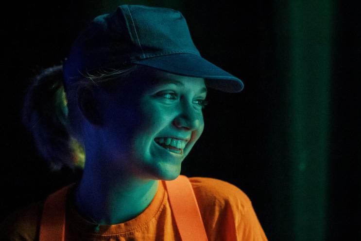 Young girl in bright orange top, smiling and enjoying being on stage.