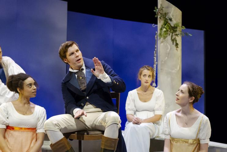 A man giving a speech surrounded by a group of women