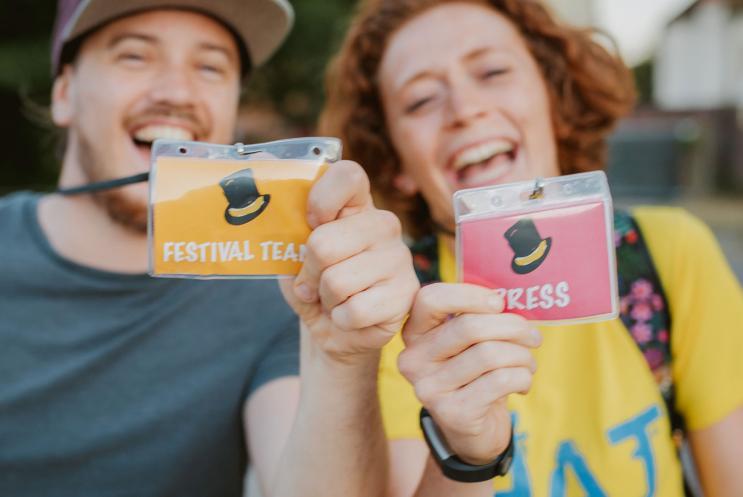 Two smiling people holding press passes up to the camera