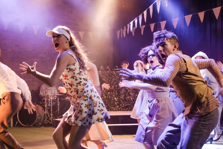 A group of people dancing on stage under multi-coloured lighting